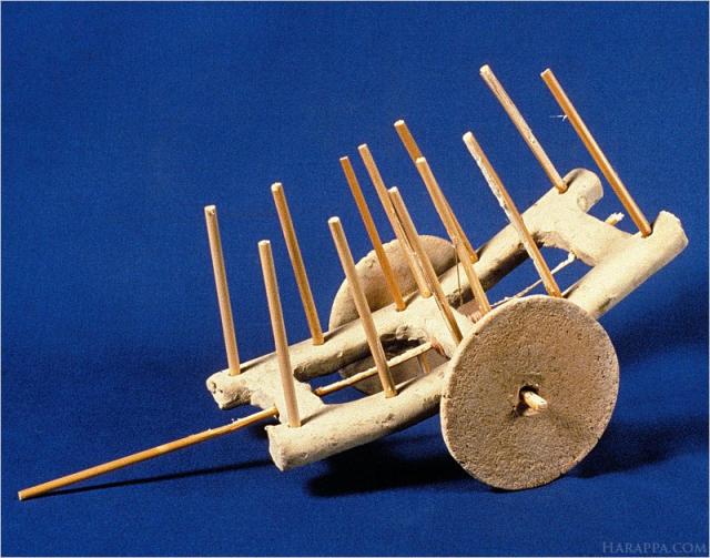 Holes along the length of the cart serve to hold wooden side bars and at the center of the cart two of the wooden side bars can be extended below the frame to hold the axle. A long stick inserted into the holes at the end of the cart would have been used to support a yoke. The two wheels were found lying next to the cart frame. Period III, Harappan, 2300-2200 B. C. Similar carts are still used in rural areas of Pakistan and India.